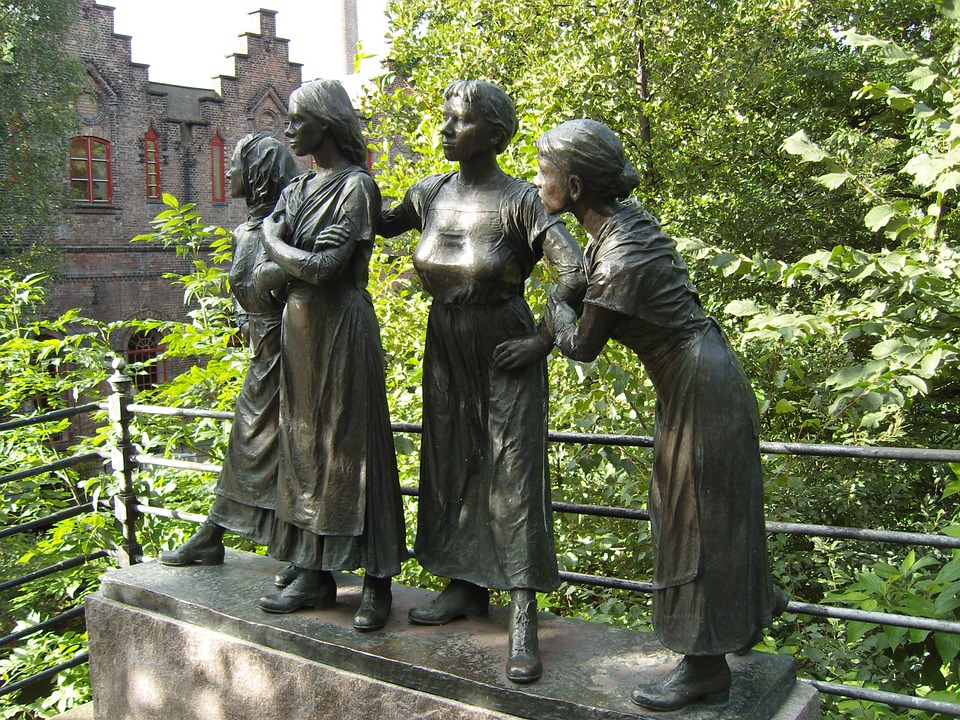 A statue of four women in dresses with green trees in the background. 