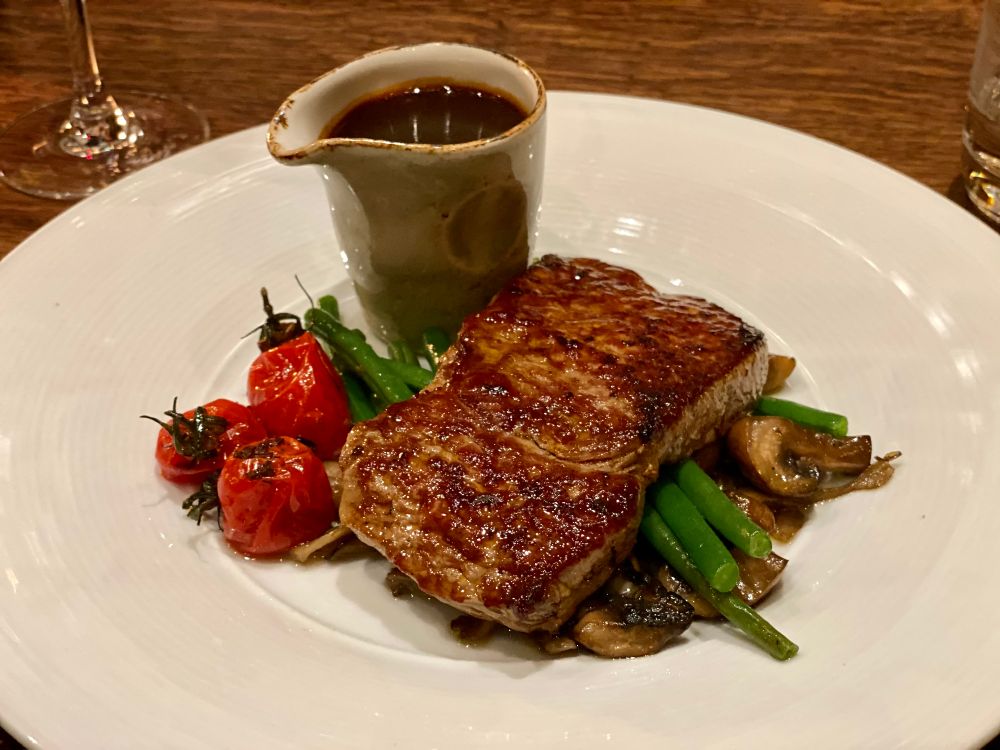 a dark steak on a white plate, with a small carafe of red wine sauce next to it, restaurant bryggeloftet in bergen, norway