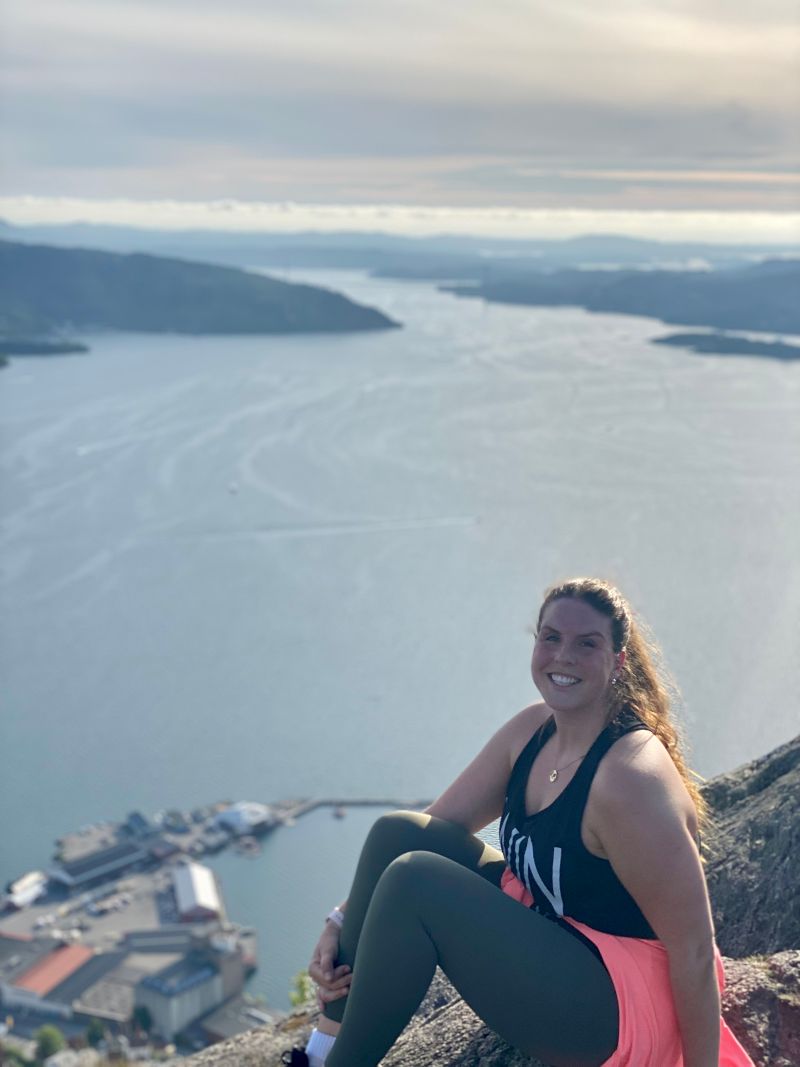 girl smiling at the camera from the top of a mountain, with the ocean and outlier islands in the background