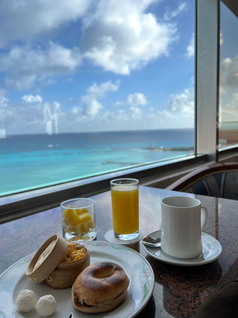 A bagel, coffee and orange juice on a table, with an ocean view background.