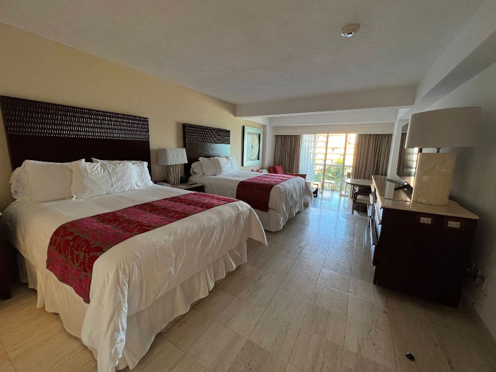 A large hotel room with two queen beds, made up with white linen and a dark red bed cover.