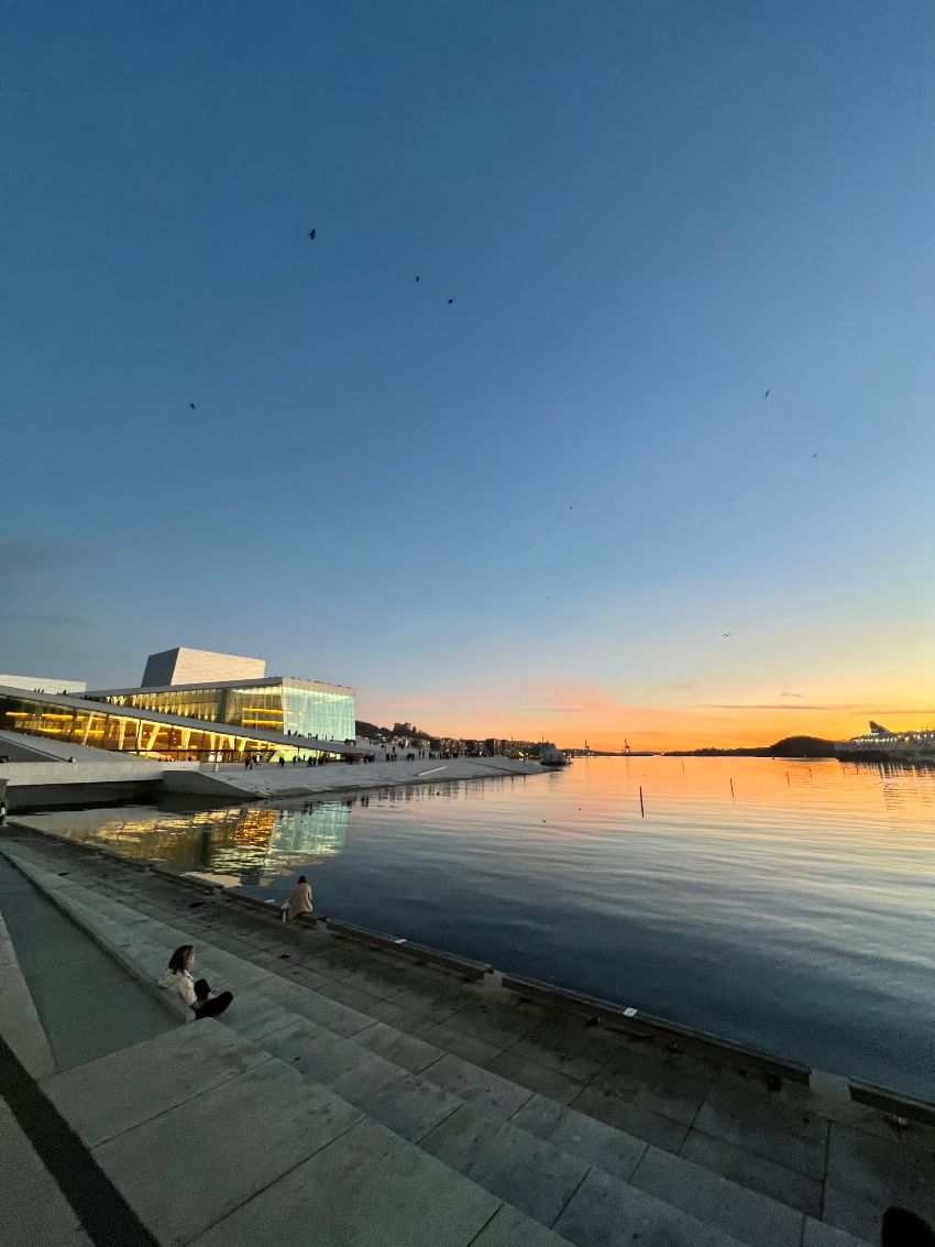 The Oslo Opera House at sunset, with a quiet fjord in front of it, and a orange sky in the background.