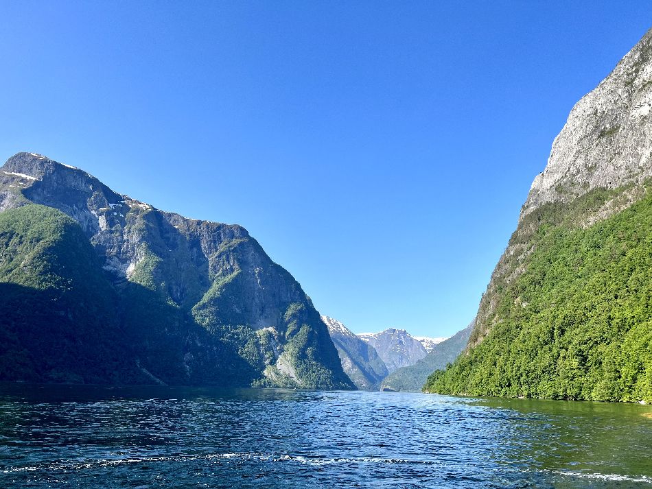 The nærøyfjord can be seen on a fjord cruise from bergen. This photo was taken on a day with beautiful weather, and the skies are all blue. There are some waves on the fjord, and the sun is shining on a mountain to the right.