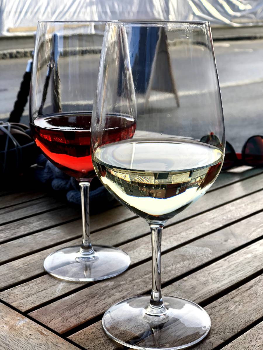 Two glasses of wine, one red, one white, on a wooden table, with a pair of sunglasses and woolen gloves in the background.