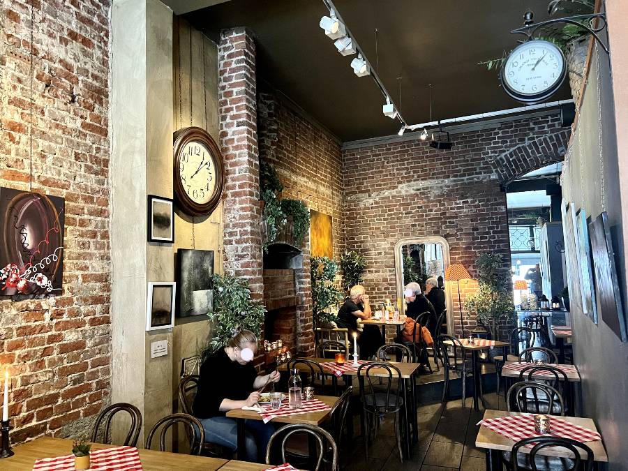 The interior of Pygmalion cafe, with exposed brick walls, local art on the walls and checked table cloths on the small tables.